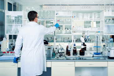 Un laborantin dans un laboratoire propre, moderne et blanc place un verre de laboratoire sur une étagère.