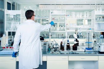 Un laborantin dans un laboratoire propre, moderne et blanc place un verre de laboratoire sur une étagère.