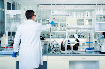 Laborant in einem sauberen, modernen, weißen Labor stellt ein Laborglas in ein Regal.