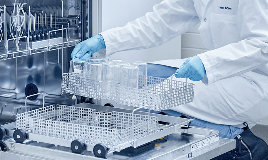 Eine Labormitarbeiterin belädt den Korb einer Spülmaschine für die maschinelle Laborglasreinigung