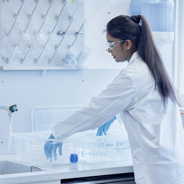 Laborantine chimique en tenue de protection, nettoyant manuellement la verrerie de laboratoire